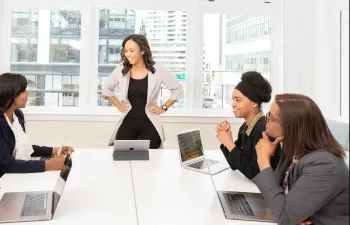 Reunión de empresa en el que todos están alrededor de una mesa escuchando a su jefa