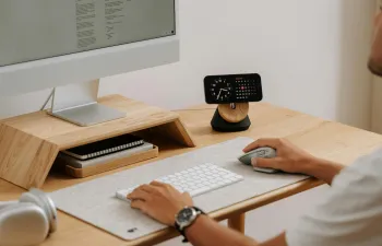 Una persona esá con su ordenador trabajando y encima de la mesa hay un reloj