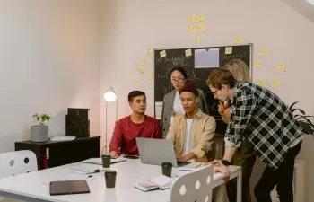 Un grupo de jóvenes están en una oficina viendo el ordenador de su compañero