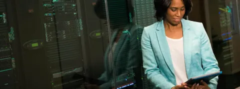 Una mujer esta apoyada en una cristalera mientras observa una tablet