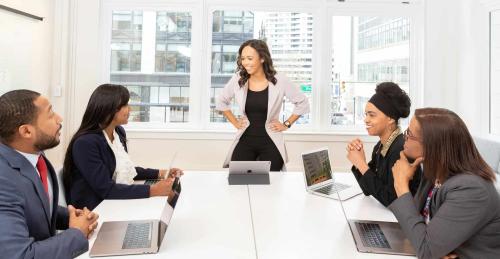 Reunión de empresa en el que todos están alrededor de una mesa escuchando a su jefa